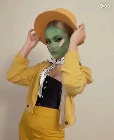 a woman wearing a yellow outfit and hat with her hands on her head while standing in front of a white wall