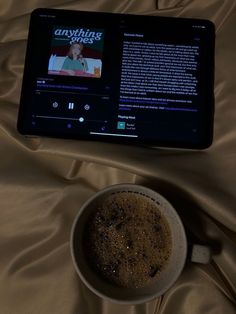 a cup of coffee sitting on top of a bed next to an electronic tablet computer