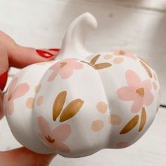 a hand holding a white pumpkin decorated with pink and gold flowers