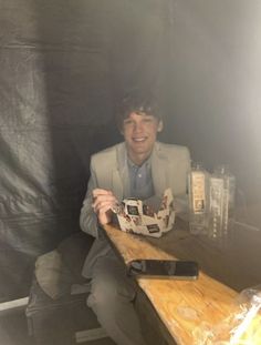 a man sitting at a wooden table holding a cup in front of him and smiling