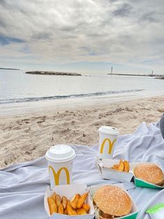 two hamburgers and french fries on a blanket at the beach with mcdonald's cups