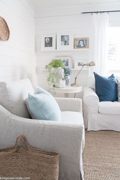 a living room filled with white furniture and pictures on the wall above it's windows