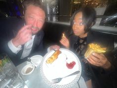 a man and woman sitting at a table with food in front of them, both eating french fries