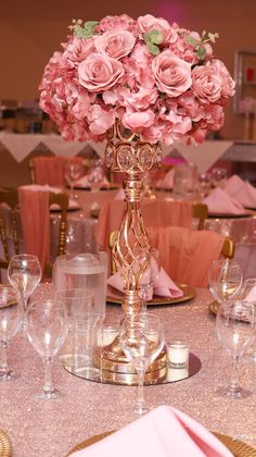 pink flowers are in a gold vase on a table with silverware and napkins