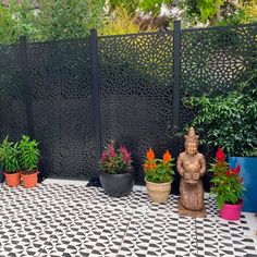 several potted plants are sitting on a black and white checkered tile floor in front of a fence