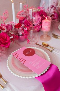 the table is set with pink flowers, candles and place settings for an elegant dinner