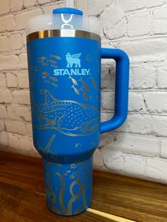 a blue travel mug sitting on top of a wooden table next to a brick wall