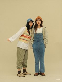 two young women standing next to each other in overalls and knitted hats, posing for the camera