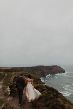 a bride and groom walking down a path towards the ocean