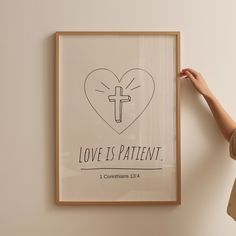 a woman holding up a framed poster with the words love is patient and a cross