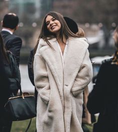 a woman in a white coat smiles as she stands next to other people on the grass