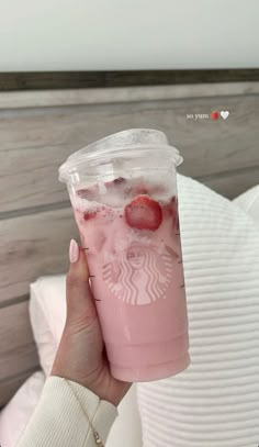 a woman holding up a pink drink with strawberries in it