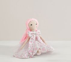 a doll with pink hair and dress sitting on the floor in front of a white wall