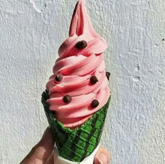 a hand holding an ice cream cone with pink icing and chocolate chips on top