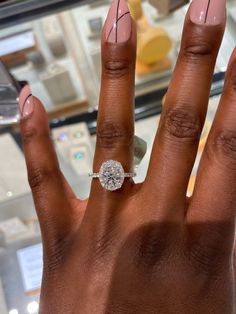 a woman's hand with a diamond ring on top of her finger, in front of a glass display case