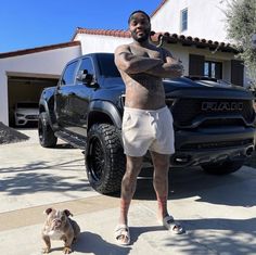 a man standing in front of a black truck next to a small dog on the sidewalk