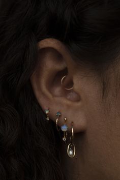 a close up of a woman's ear wearing gold earrings with opal stones