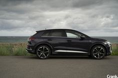 a black car parked on the side of a road next to water and grass with storm clouds in the background