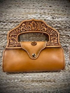 This little purse is stunning! The color is a beautiful golden brown with a matching closure. The handle is completely hand tooled. It  is made from Herman Oak top grain leather and is hand stitched all around to insure it will not lose it's shape. The bottom is made from Wickett & Craig harness leather. This type of leather has waxes and oils forced into the leather during the tanning process. This makes it more waterproof. The bottom has also been hand stitched. The size of this purse is 8 inc Brown Hand-tooled Wallets For Everyday Use, Hand Tooled Bifold Clutch For Everyday Use, Handheld Brown Leather Wallet, Hand Tooled Coin Purse, Leather Handbags Diy, Handbags Diy, Leather Craft Projects, Fall Bags, Leather Carving