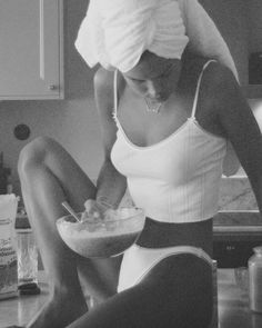 a woman sitting on the kitchen counter mixing something in a bowl while wearing a towel over her head