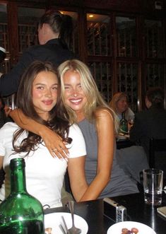 two beautiful young women sitting next to each other in front of a table with food and drinks