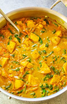 a pot filled with curry and tofu on top of a marble counter next to a wooden spoon