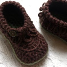 a pair of brown crocheted baby shoes sitting on top of a white blanket