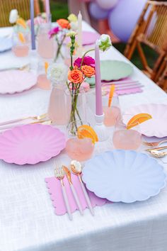 the table is set with pink and blue plates, silverware, candles, and flowers