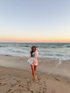 a woman is walking on the beach at sunset