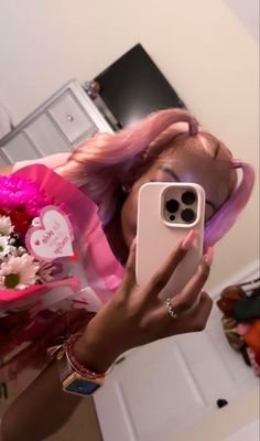 a woman taking a selfie with her cell phone in front of her face and flowers behind her head