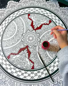 a person is painting on a large white doily with red paint and black ink