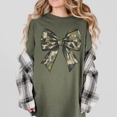 This stylish camoflauge bow t-shirt is the perfect blend of edgy and feminine fashion. The unique camoflauge print adds a touch of military-inspired trendiness, while the bow detail on the front brings a cute and playful touch. Made from soft and comfortable fabric, this t-shirt is ideal for everyday wear or for adding a statement piece to your outfit. Stand out from the crowd with this eye-catching camoflauge bow t-shirt! SIZE UP 1-2 SIZES FOR AN OVERSIZED LOOK! Thanks so much for shopping with Camouflage T-shirt For Fall, Fall Camouflage Tops With Graphic Print, Fall Cotton Top With Bow Detail, Wife T Shirt, Feminine Fashion, Army Wife, Military Wife, Coquette Bow, Wife Gift