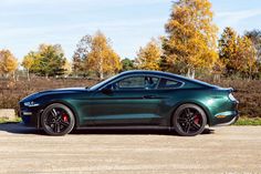 a green mustang parked on the side of a dirt road in front of some trees