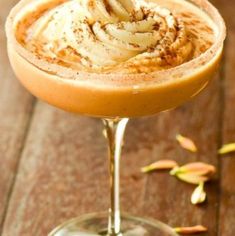 an orange drink with whipped cream on top in a coupe glass sitting on a wooden table