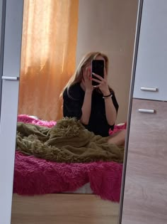 a woman taking a selfie while sitting on a bed in front of a mirror