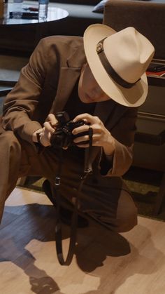 a man sitting on the floor with a camera in his hand and wearing a hat