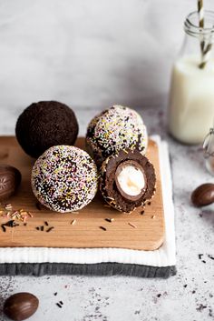 chocolate covered donuts with sprinkles on a cutting board next to a glass of milk