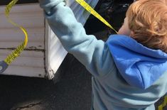 a young boy measuring the length of a truck with yellow tape on it's side