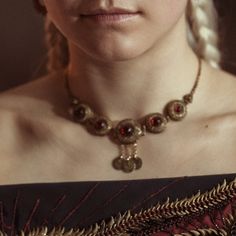 a woman with braids wearing a red dress and a necklace on her neck is looking at the camera