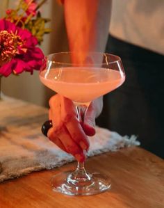 a person holding a wine glass on top of a wooden table with flowers in the background