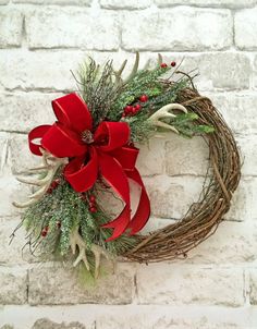 a christmas wreath on a brick wall with red bow and antler sprigs