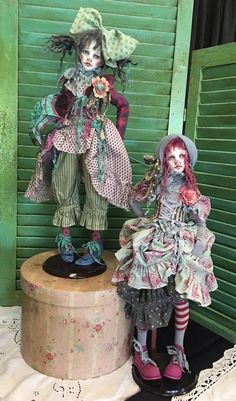 two creepy dolls are standing next to each other on a round table in front of green shutters