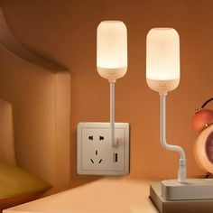 an alarm clock sitting on top of a table next to two plugs and a lamp