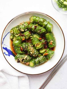 a white plate topped with green vegetables covered in sauce and seasoning next to chopsticks