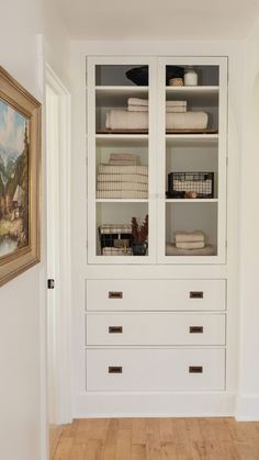 an empty room with white cabinets and wood floors in front of a painting on the wall