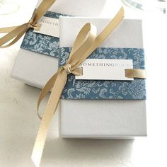 two wrapped gift boxes sitting on top of each other with ribbons tied around the edges