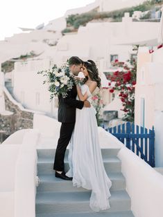 a bride and groom kissing on the steps in front of white buildings with blue railings