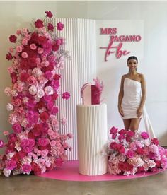 a woman standing next to a tall white vase with pink flowers on it's side