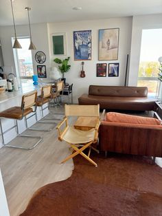 a living room filled with furniture next to a kitchen and dining room table in front of a large window