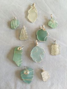 seven sea glass pendants sitting on top of a white cloth covered table next to each other